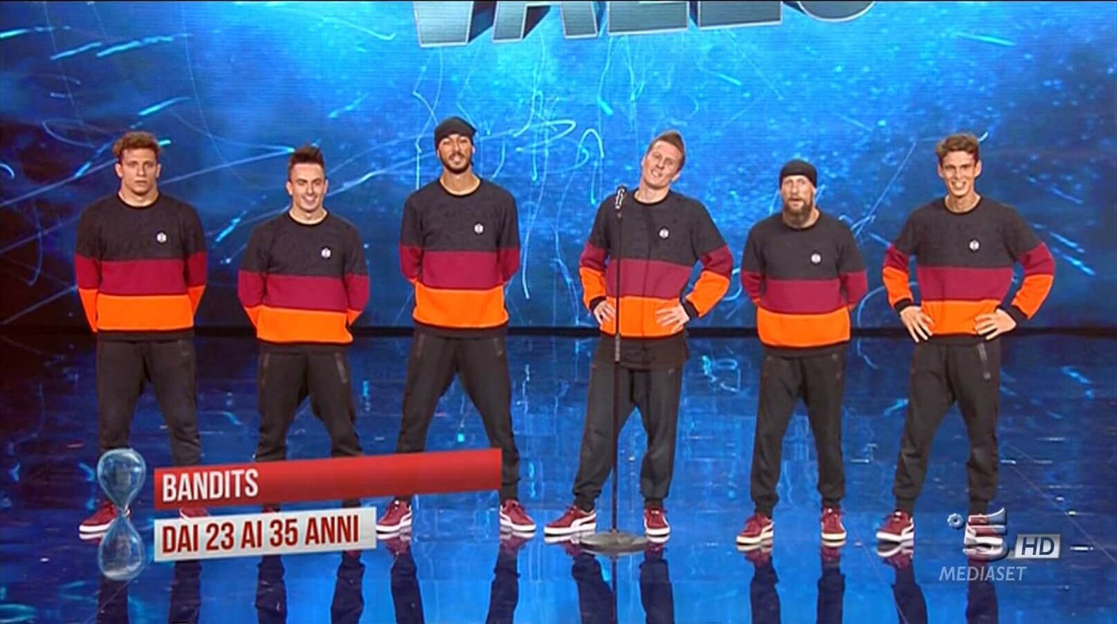 Gruppo maschile in posa su palco televisivo.