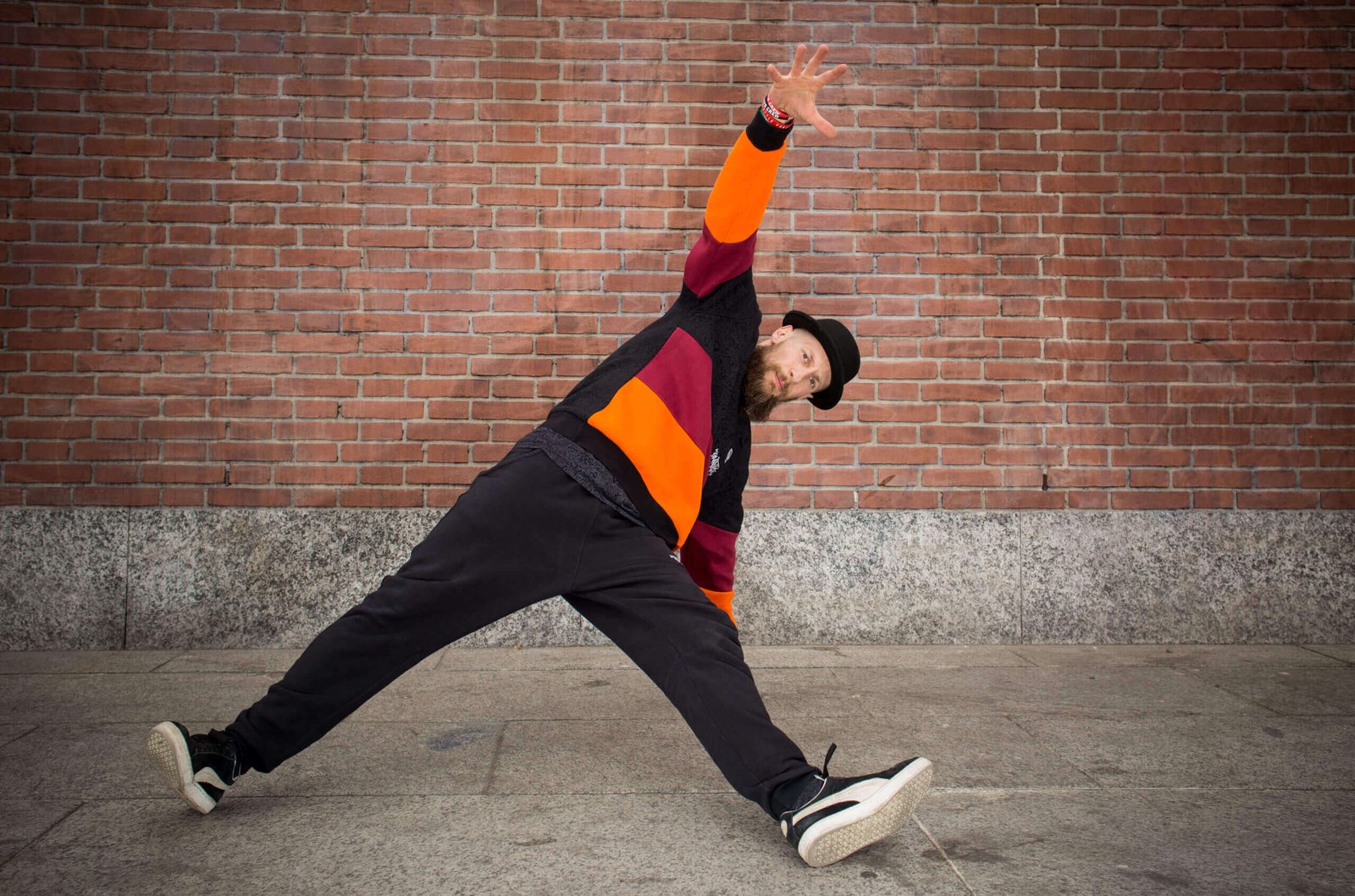 Uomo che balla hip-hop davanti a muro di mattoni.